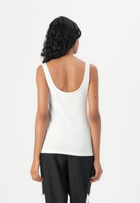 Bílý bezrukávový top s zaobleným výstřihem na zádech, hladkou tkaninou, přiléhavým designem a minimálním šitím, spojený s černými volnými kalhotami.