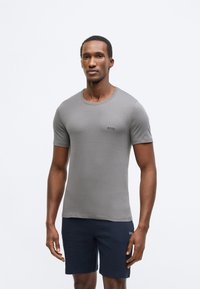 Šedé tričko s krátkým rukávem z měkké látky, s kulatým výstřihem a jemně vyšívaným logem na levé straně hrudi.