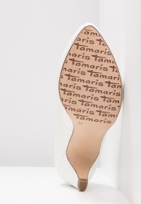 Weißer High-Heel-Schuh mit spitz zulaufender Spitze. Glattes Lederobermaterial, minimalistisches Design, braunes Logo auf der Sohle, Größe 37 gekennzeichnet.