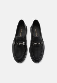 Mocassini neri con tomaia texturizzata, decorati con una catena in argento e punta arrotondata. Suola liscia per una maggiore comodità.