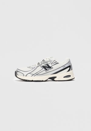 Baskets New Balance 740 blanches et grises avec empeigne en mesh, logo noir "N" et semelle rembourrée sur fond gris clair.