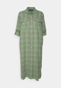 Robe chemise longue à carreaux verts avec manches retroussées, boutonnée sur le devant et deux poches à rabat sur la poitrine.