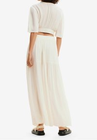Světle zbarvený dvoudílný outfit skládající se z krátkého topu s krátkými rukávy a dlouhé, splývavé sukně vyrobené z texturované tkaniny.