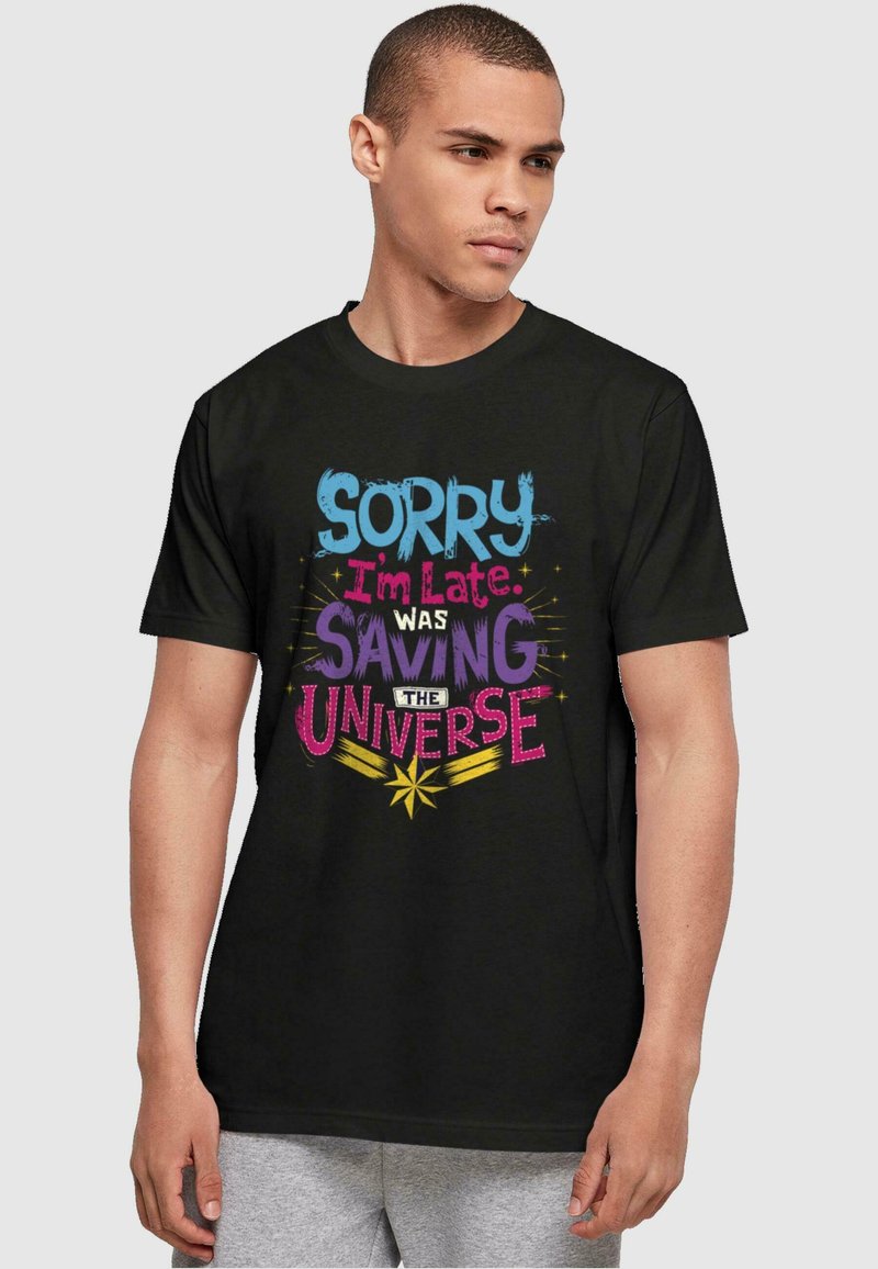 Camiseta de algodón negra con texto colorido: "Lo siento, llego tarde, estaba salvando el universo" junto a estrellas y un diseño gráfico llamativo.