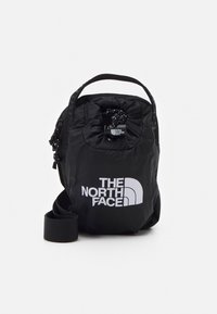 Borsa a tracolla in nylon nero con apertura a cordoncino, tracolla regolabile e grande logo bianco. Texture liscia, design compatto per l'uso quotidiano.