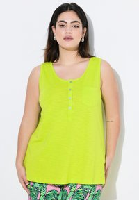 Top sin mangas de color verde lima con escote redondo, tapeta frontal de cinco botones y un bolsillo en el pecho. Textura suave y diseño de corte relajado.