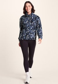 Navy and black pullover with a cowl neck and speckled print. Paired with black leggings and white athletic shoes. Smooth, soft texture.