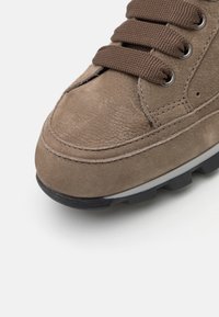 Baskets en daim marron avec bout arrondi, couture renforcée et semelle extérieure en caoutchouc foncé avec crampons de traction proéminents ; fermeture à lacets avec lacets plats.