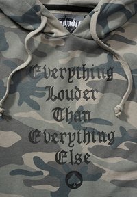 Felpa con cappuccio grigia in camouflage con un cordoncino, caratterizzata da un testo audace che recita "Tutto più forte di tutto il resto" in nero, con il logo a forma di piccone.
