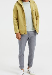 Yellow waterproof jacket, light green t-shirt, grey patterned trousers, white sneakers with black accents, relaxed fit, casual design.