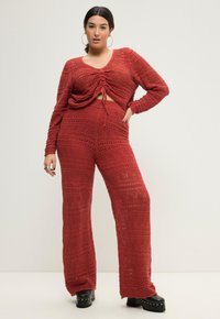 Set in maglia a uncinetto rosso composto da due pezzi, caratterizzato da una maglietta a maniche lunghe con nodo frontale e pantaloni larghi con pattern testurizzati e una vestibilità rilassata.
