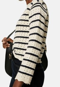Prążkowany sweter z dzianiny w kolorach kremowym i granatowym, z teksturowanym wzorem i oczkowymi detalami. Krótki, z okrągłym dekoltem i długimi rękawami.