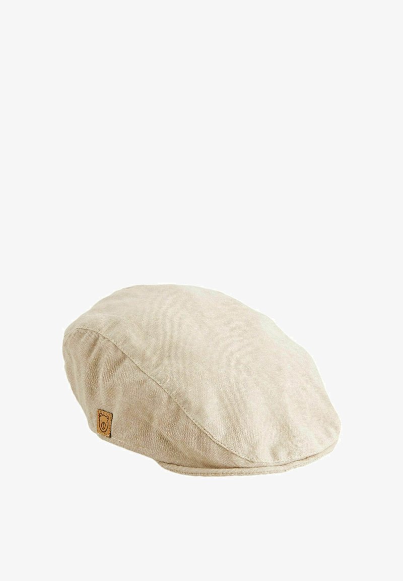 Beige linnen flat cap met ronde vorm, stiksel detail en een klein merklabel met een berenembleem. Zachte textuur, casual ontwerp.