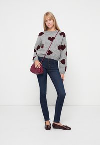 Sivi pulover s burgundskim uzorcima srca, plave uske traperice i burgundska torbica preko tijela. Sjajne crne balerinke završavaju outfit.