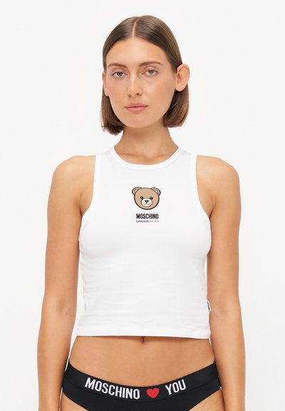Biała krótka bluzka na ramiączkach z okrągłym dekoltem, z grafiką misia i napisem "MOSCHINO UNDERBEAR". Noszona z czarnymi majtkami z wysokim stanem.
