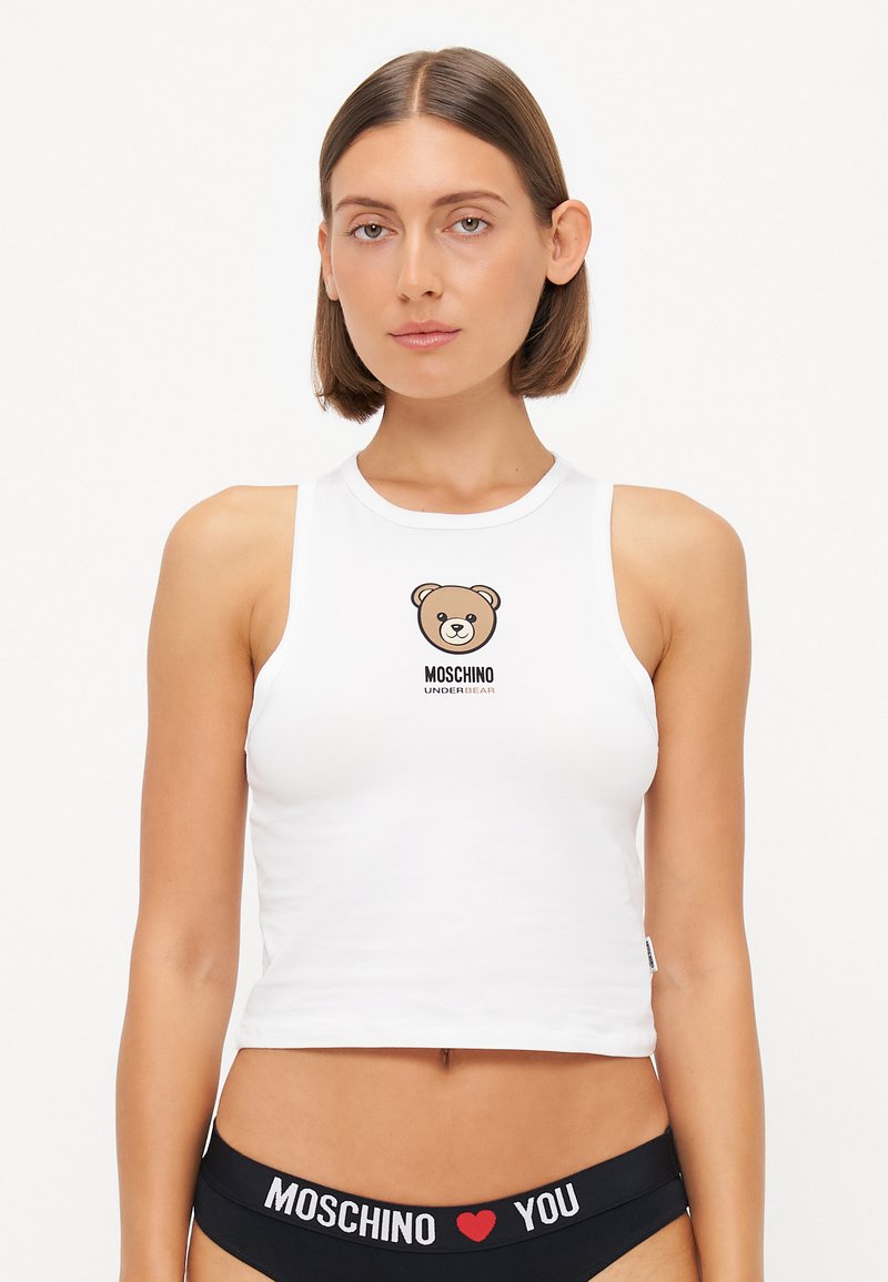 Biely skrátený top bez rukávov s okrúhlym výstrihom, zdobený grafiku medveďa a textom "MOSCHINO UNDERBEAR". Oblečené s čiernym spodným prádlom s pásom.