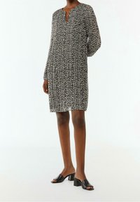 Robe imprimée léopard en tissu léger, avec un col en V, des manches longues et une coupe décontractée. Associée à des mules à talons carrés ouverts noires.