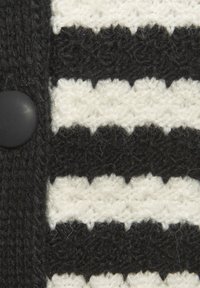 Knit tkanina u crno-bijelim prugama s teksturiranim uzorkom i crnim plastičnim gumbom na rubu.