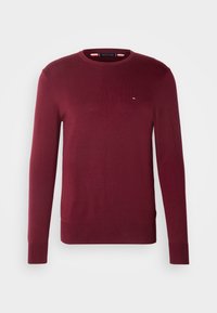 Pull à manches longues et col rond en bordeaux avec poignets et ourlet côtelés, arborant un petit logo rouge, blanc et bleu sur la poitrine gauche.