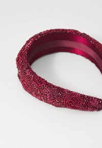 Fascia per capelli in rosso scuro, caratterizzata da motivi floreali in rilievo e retro in satin liscio, con forma arrotondata e hardware decorativo.