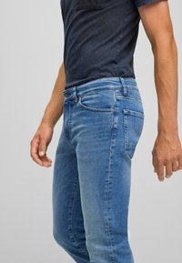 Světle modré džíny z denimu s úzkým střihem, designem s pěti kapsami, viditelnými švy a tmavým akcentem na kapse na levé straně.