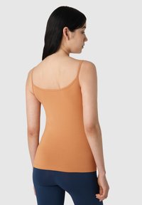 Top de tanque naranja con tirantes finos, diseño ajustado, textura suave y escote redondeado, combinado con leggings azul oscuro.