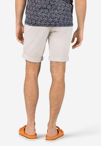 Men's rolled cuff beige shorts, lightweight fabric, paired with orange slip-on shoes. Background is plain white, highlighting attire details.