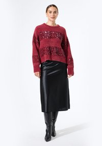 Suéter de punto burdeos con rayas de lentejuelas, combinado con una falda midi de satén negra y botas negras hasta la rodilla. Fondo liso.