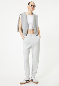 Grå sweatshirt med ærmeløst design, hvid crop top, grå sweatpants og hvide sneakers med sorte detaljer. Glatte teksturer hele vejen igennem.