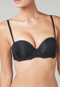 Reggiseno nero con ferretto, coppe imbottite, bordo in pizzo sulla fascia, spalline regolabili e un piccolo fiocco al centro. Tessuto morbido.