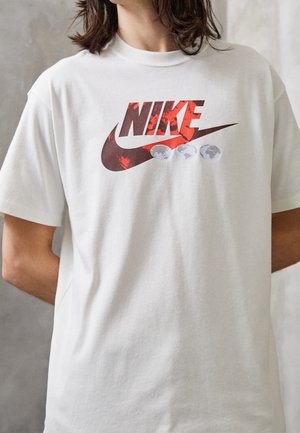 Biała bawełniana koszulka z dużym czerwono-czarnym logo Nike oraz trzema szarymi ikonami globu pod logo. Krótkie rękawy, okrągły dekolt.