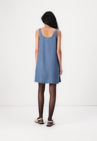 Denim ermløs kjole med rund hals, åpning på ryggen og rå kant. Brukes med svarte strømpebukser og lyse sandaler.