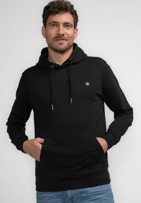 Sudadera con capucha negra hecha de una tela suave, con un bolsillo tipo canguro, cordones ajustables y un pequeño logo en el pecho.