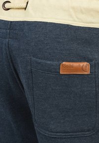 Dark blue hoodie fabric with a cream drawstring, featuring a leather tag labeled "Solid" on the right pocket. Classic pullover design.