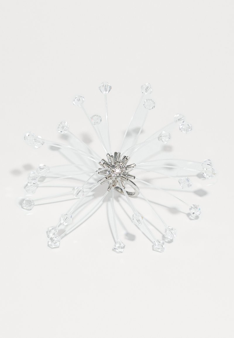 Kristály bross ezüst színű fémből, átlátszó gyöngyökkel vékony drótokon elrendezve, csillagrobbanás mintát adva, kiemelve az átlátszóságot és a fényvisszaverődést.