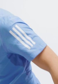 Ljusblå sporttröja med korta ärmar och tre vita vertikala ränder på axeln. Tillverkad av ett mjukt tyg med en figursydd design.