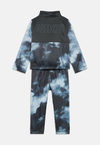 Conjunto desportivo Nike com um design em tie-dye preto e azul. A jaqueta tem um colarinho alto e um grande logótipo; as calças são ajustadas com um cós elástico.