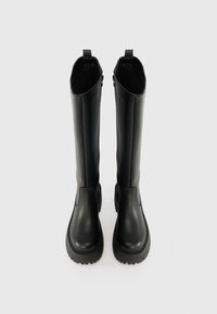 Crne čizme do koljena od glatke kože, s okruglim prstima, debelim teksturiranim potplatom i petljama na vrhu. Bočni zipovi.