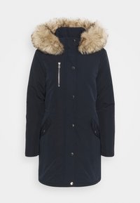 Navy parka jacket with a faux fur hood, zip pocket, side pockets, snap button closure, and quilted texture. Suitable for cold weather.