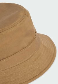 Cappello a secchiello khaki in cotone con una larga visiera cucita e una consistenza liscia. Caratterizzato da una corona senza cuciture e da un sottile dettaglio a coste.