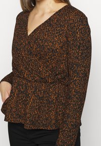 Blusa nera e arancione con motivo a fantasia, scollatura a V, maniche lunghe e vita a peplo, realizzata in un tessuto testurizzato.