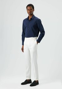 Chemise boutonnée bleu marine, pantalon blanc sur mesure et chaussures à enfiler en suède noir. Design simple, texture lisse et palette de couleurs neutres.