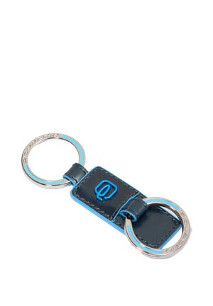 Leren sleutelhanger met twee zilveren ringen, zwart gestikte middenpaneel en blauw logodetail op een witte achtergrond.