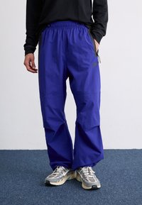 Pantalones morados de corte holgado con una cintura elástica y bolsillos laterales. Hechos de un material suave con un ligero brillo, con un detalle de logo.