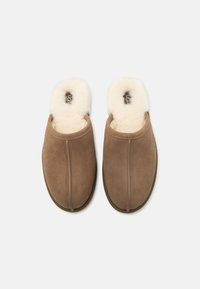 Paire de chaussons marron en daim à enfiler avec doublure intérieure blanche et duveteuse, vue de dessus sur un fond clair.