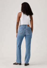 Jeans taille haute bleu clair en denim, présentant un design de poche arrière, une patte en cuir à la taille et une coupe droite.