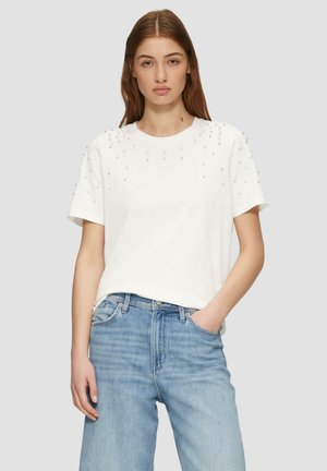 Witte katoenen T-shirt met verhoogde kralenaccenten op de schouders, ronde halslijn en korte mouwen, gecombineerd met lichtgewassen denim jeans.