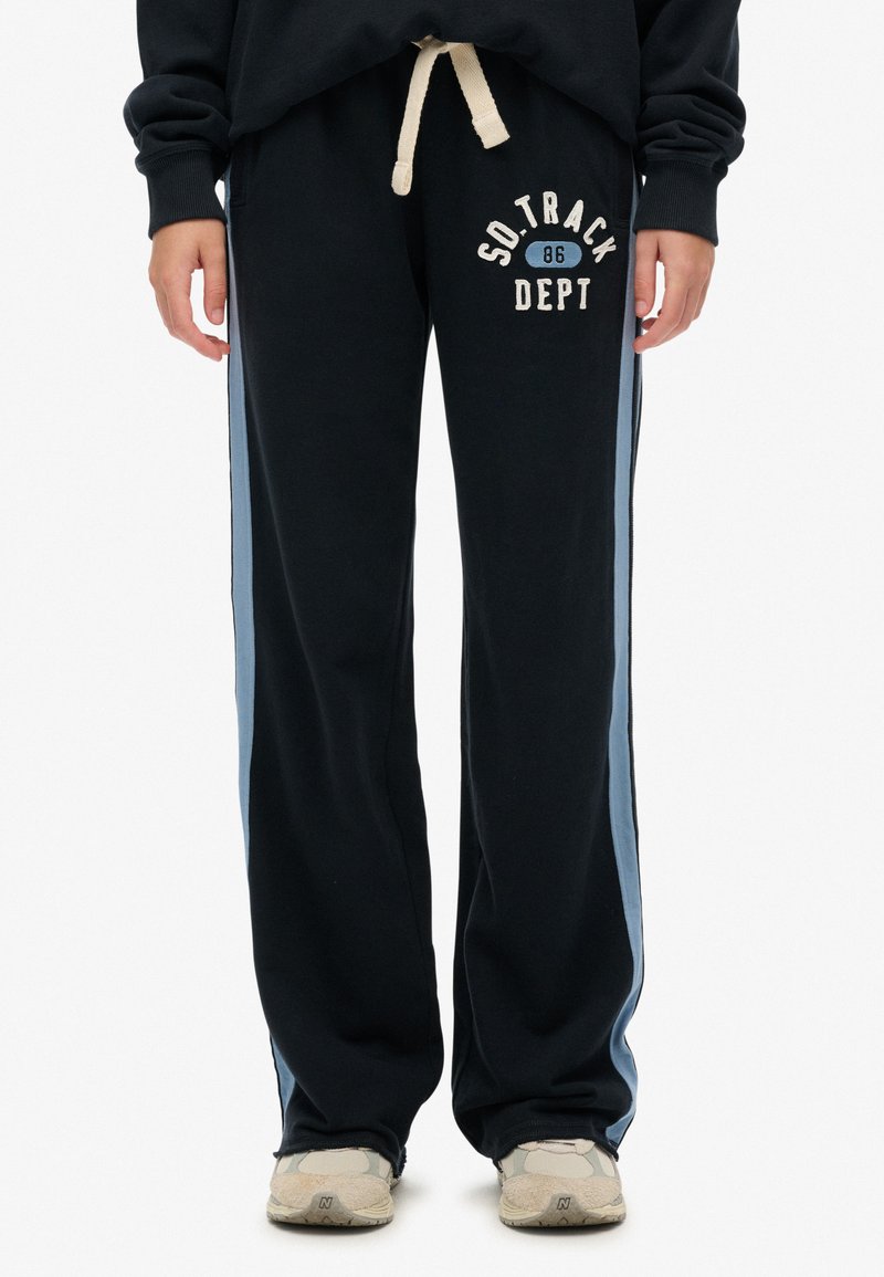 Zwarte joggingbroek met blauwe zijstrepen, voorzien van een trekkoord in de taille en "SO TRACK DEPT 86" bedrukt aan de voorkant. De stof lijkt zacht.