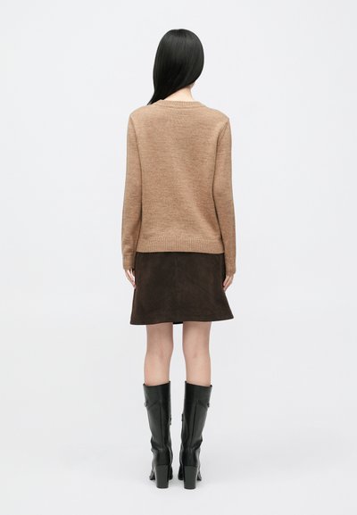 Rjav pulover iz pletenine z okroglim izrezom in rebrastimi manšetami, kombiniran z rjavo semiš krilo. Model nosi črne škornje do kolen.