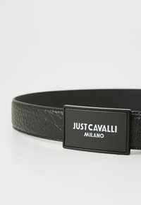 Črn usnjen pas z teksturiranim zaključkom in pravokotno sponko z izbočenim belim logotipom "JUST CAVALLI MILANO."